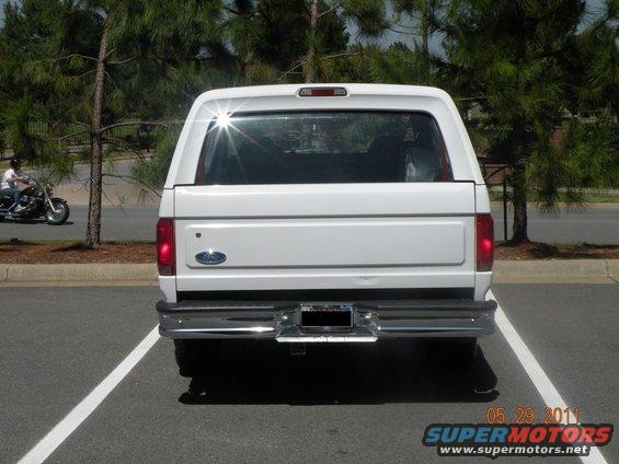 White Ford Bronco parked in a parking lot, rear view. Chrome bumper and license plate visible