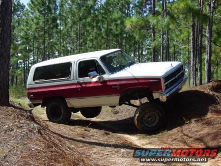 White and red SUV with lifted suspension off-roading on a dirt path