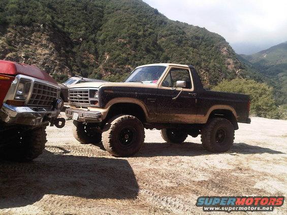Brown and tan 1980s Ford Bronco with lifted suspension, parked next to another truck