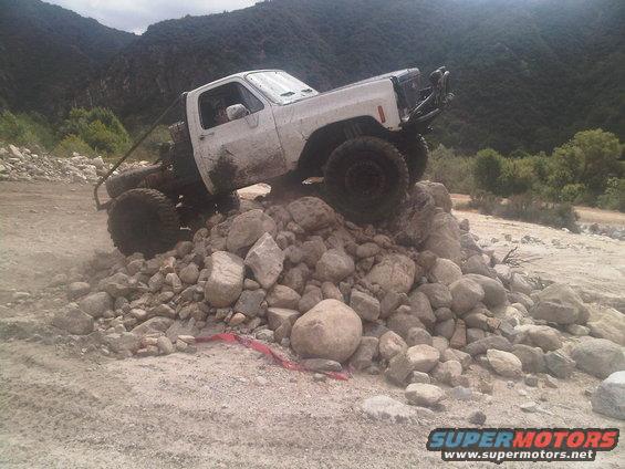 White pickup truck with off-road modifications climbing over a pile of rocks
