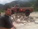 1986 Ford Bronco - A man stands in front of a red pickup truck that is positioned on a rocky incline in a natural setting.