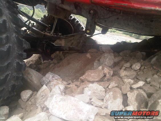 Red vehicle undercarriage with large tires stuck in rocks