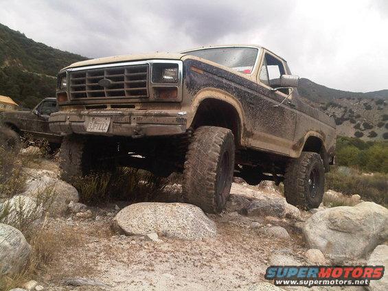 Tan and brown Ford Bronco with lifted suspension and large tires on rocky terrain