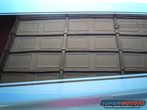 Overhead garage door with four rows of panels, some warped, with a blue car reflection below