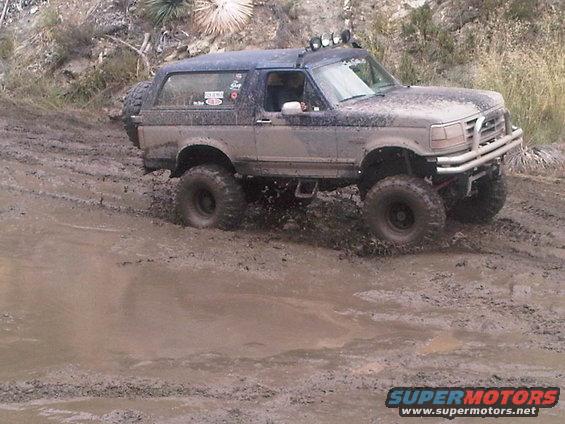 Mud-covered 1992-1996 Ford Bronco driving through a muddy trail with large off-road tires