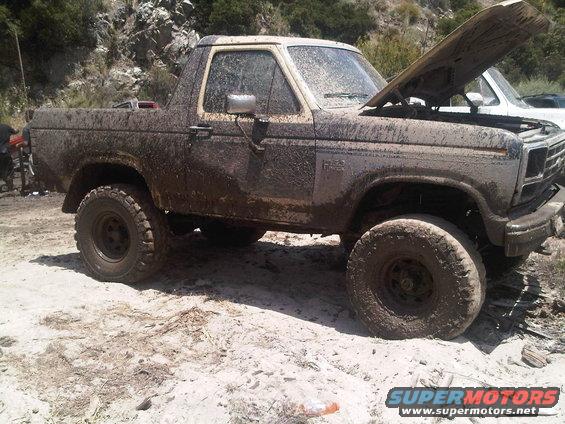 Muddy SUV with hood up, parked on dirt. Another vehicle is partially visible behind it