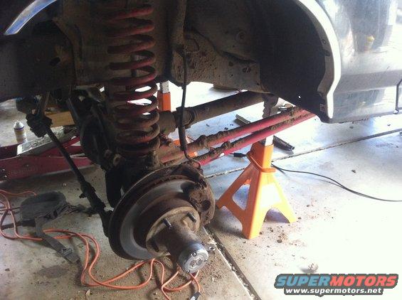 Undercarriage of a lifted vehicle on jack stands, showing suspension components and a brake rotor