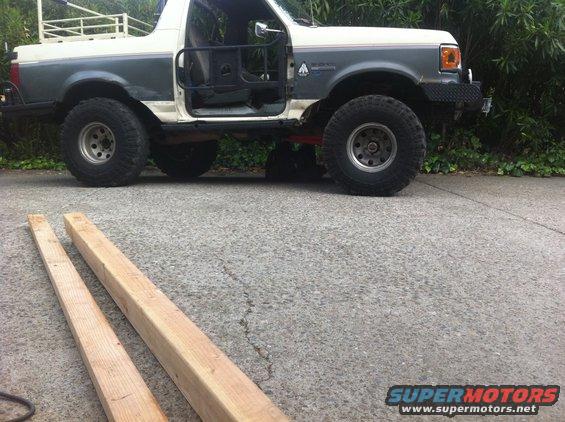 Two-tone gray and white Ford Bronco with lifted suspension and off-road tires, driver's door removed
