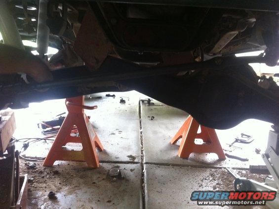 Undercarriage of a lifted vehicle on jack stands, showing suspension and drivetrain components