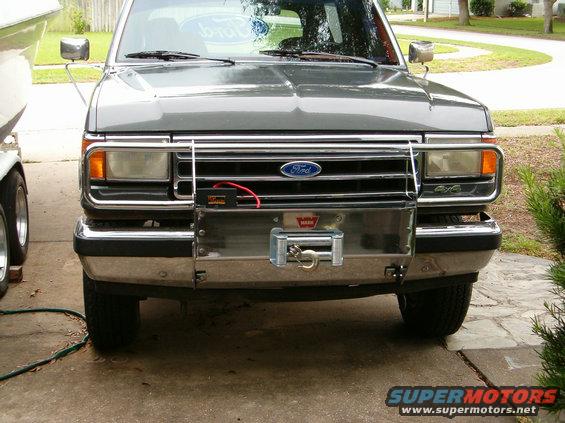 Front view of a gray Ford Bronco with a chrome grille guard and a winch mounted on the bumper. It has a "4x4" badge on the fender