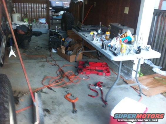Garage scene with a person working on a vehicle, tools scattered on the floor and a table