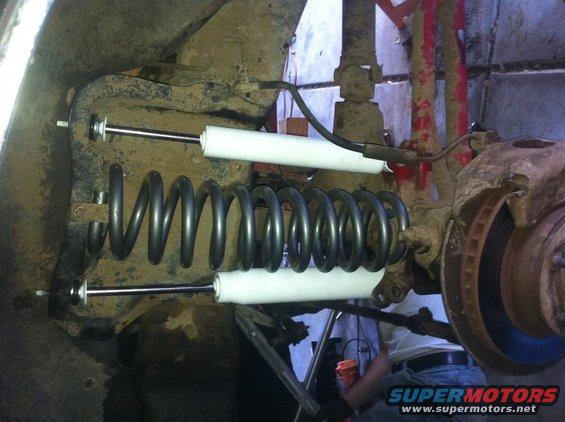 Suspension coil and shock absorbers on a vehicle's undercarriage. Rusty metal and dirt are visible
