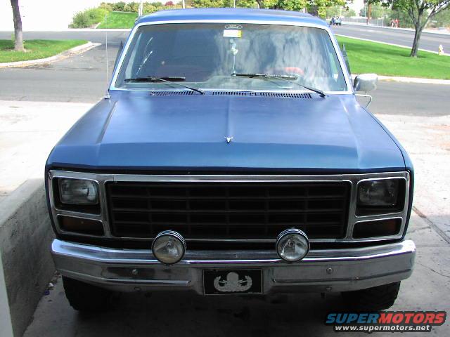 Front view of a blue pickup truck with a black grille and two round fog lights. It has a chrome bumper and a small badge below the grille