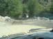 1986 Ford Bronco - Another vehicle navigates a water crossing on a dirt road surrounded by trees and rocky terrain.
