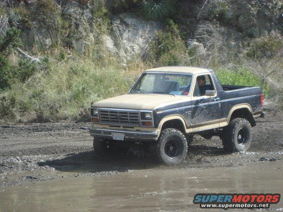 Ford Bronco with two-tone paint driving on a muddy trail