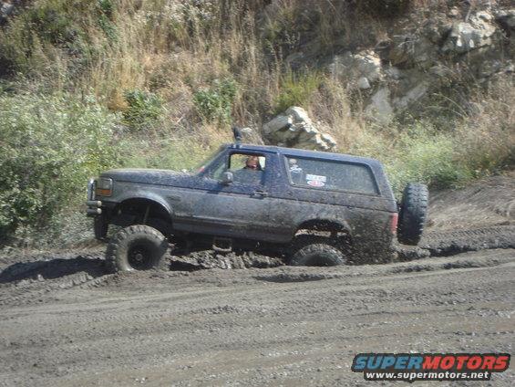 Mud-covered blue Ford Bronco stuck in thick mud, side view