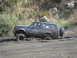 1986 Ford Bronco - A blue Ford Bronco navigates a muddy off-road trail, with its tires deeply embedded in the mire.