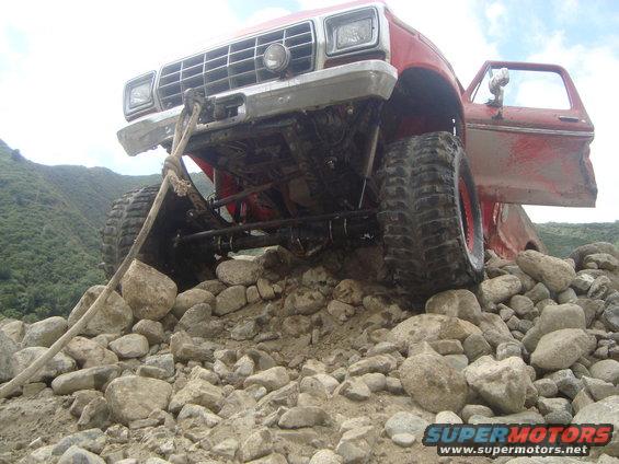 Red off-road truck with open door, front view, stuck on rocks