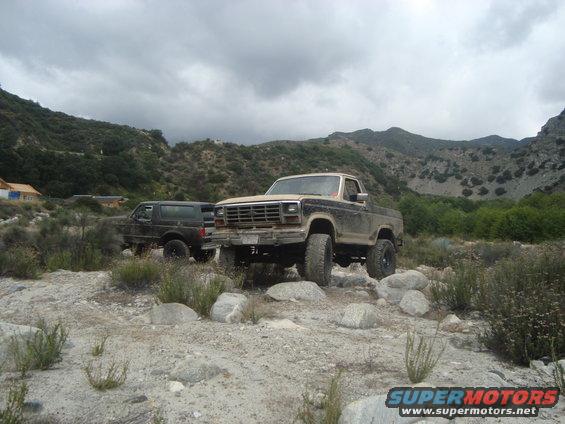 Ford pickup truck and Bronco parked on rocky terrain with mountains in background