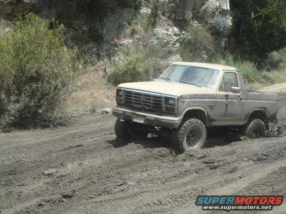Tan Ford Bronco driving through mud, 1980s model