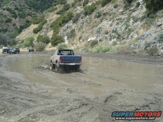 Bronco driving through mud pit with other SUVs behind it