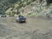 1986 Ford Bronco - Off-road vehicles navigate a muddy track in a hilly, arid landscape.