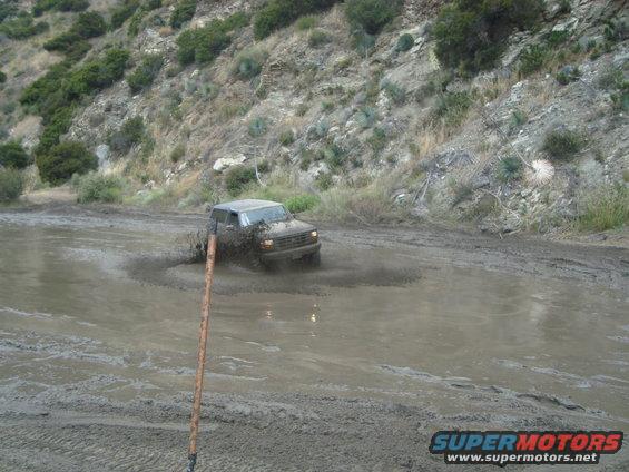 Mud-splattered dark SUV driving through a muddy puddle on a dirt road