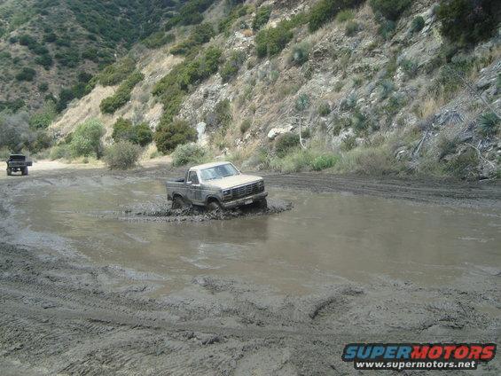Tan pickup truck stuck in mud puddle, another vehicle in background