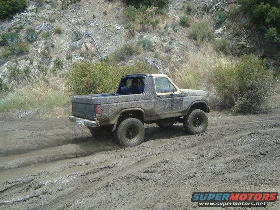 Muddy SUV driving through a dirt track with hills in background