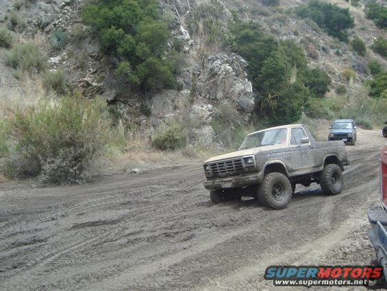 Mud-covered 1980 Ford F-150 pickup truck with off-road tires driving on a dirt road