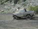 1986 Ford Bronco - This vehicle is covered in mud as it navigates a challenging off-road terrain.