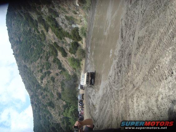 Line of off-road vehicles navigating a muddy trail with steep hillsides