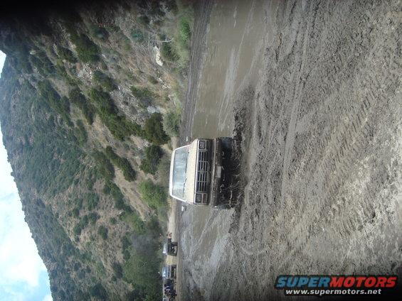 Several off-road vehicles driving through a muddy track with a hillside in the background