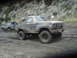1986 Ford Bronco - Two muddy Ford Broncos navigate a dirt track on a hillside.