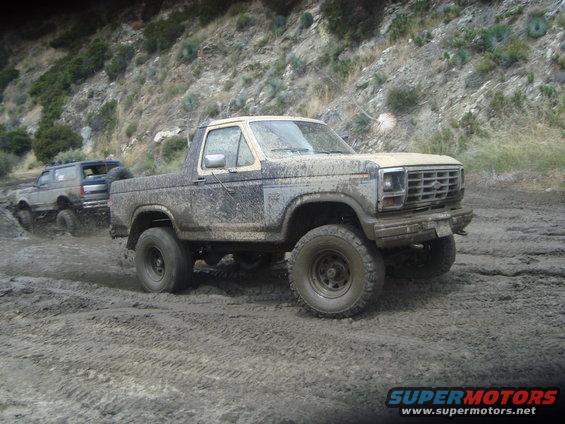 Mud-covered 1986 Ford Bronco driving through mud with another Bronco behind it
