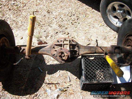 Rear axle assembly with yellow shocks and tires, resting on the ground