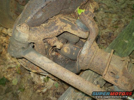 rusted vehicle axle components, including tie rod ends and steering knuckle parts, lying on the ground