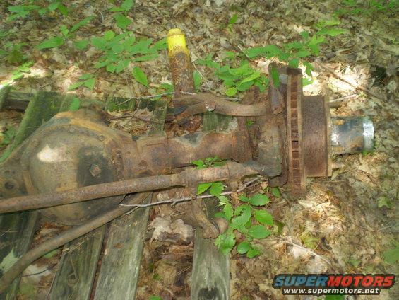 rusty axle assembly with shock absorber and brake rotor, sitting on wooden planks in woods