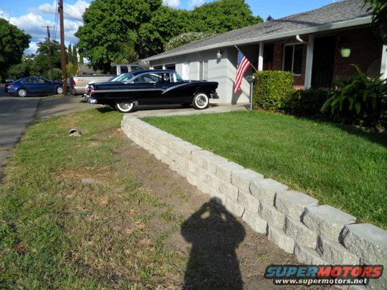 Black 1955 Ford Crown Victoria parked in front of a house with an American flag