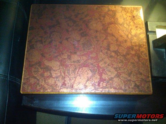 Box with marbled copper-like lid on a dark surface next to black leather