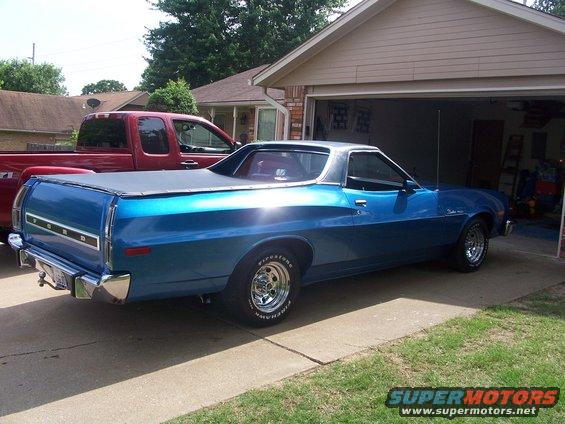 Blue 1972 Ford Ranchero with a black tonneau cover parked in a driveway next to a red pickup truck