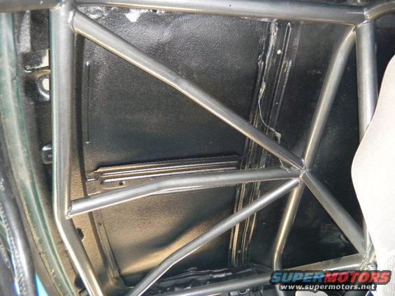 Roll cage inside a vehicle's interior, with black textured flooring and a partial view of a white seat
