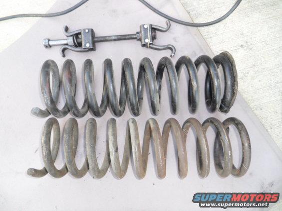 Two sets of coil springs and a spring compressor tool on a flat surface