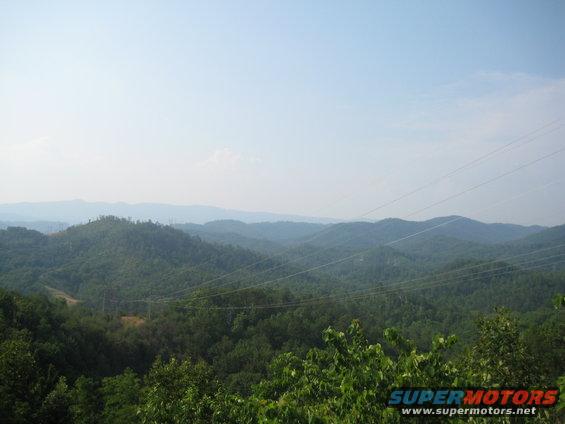 View of rolling green mountains under a clear blue sky with power lines stretching across