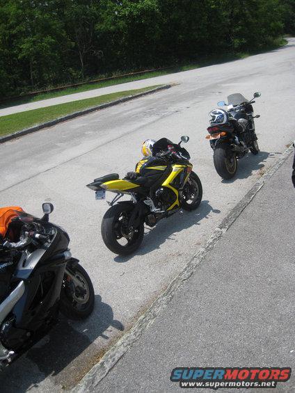 Three sport motorcycles parked on the side of a road, two yellow and black, one black