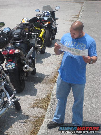 Man in blue shirt and jeans looks at a map next to a line of parked motorcycles