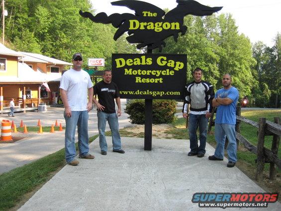 Four men stand on a concrete path before a large black dragon sign and a black sign for Deals Gap Motorcycle Resort