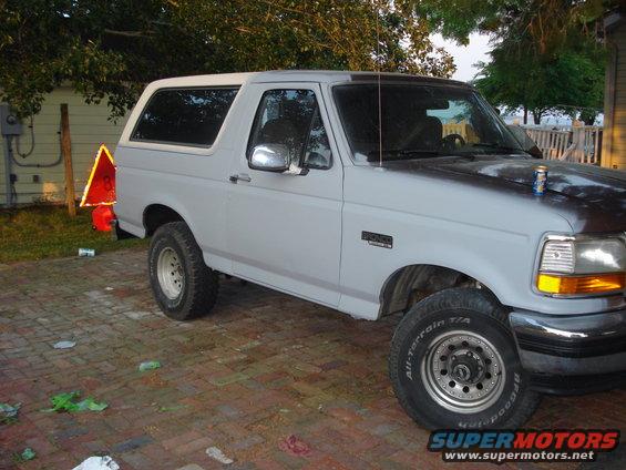 Ford Bronco parked on brick driveway, primer gray paint, some rust on hood