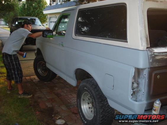 Gray Ford Bronco with white removable top, undergoing bodywork, viewed from the rear passenger side