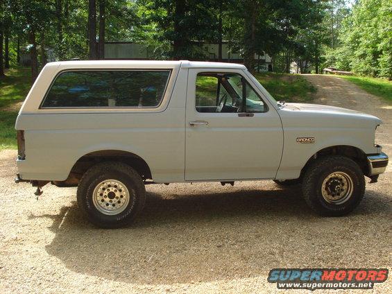 1993 Ford Bronco side view, light gray paint, tan top, parked on gravel